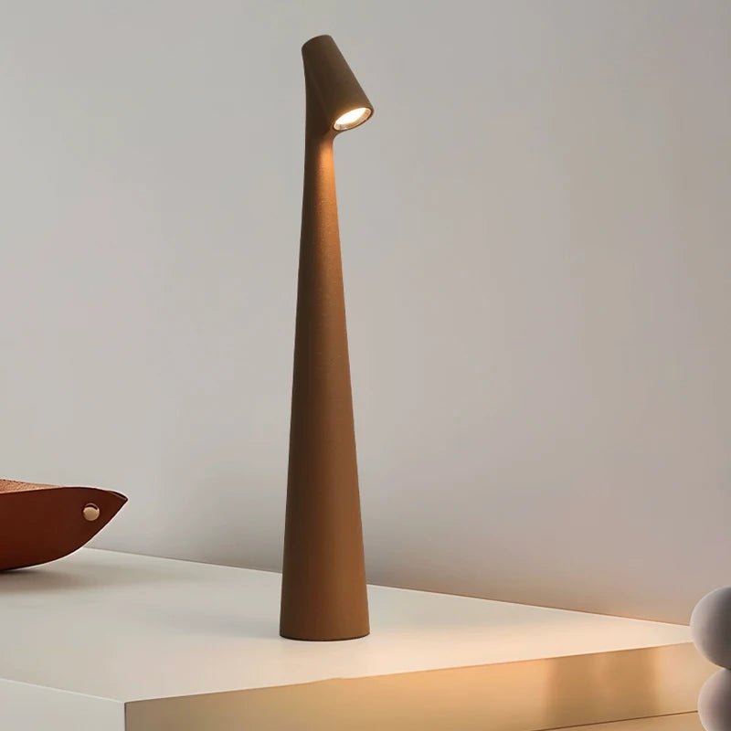 A sleek, modern, brown lamp with a narrow, tall base and a small light at the top, standing on a white surface.