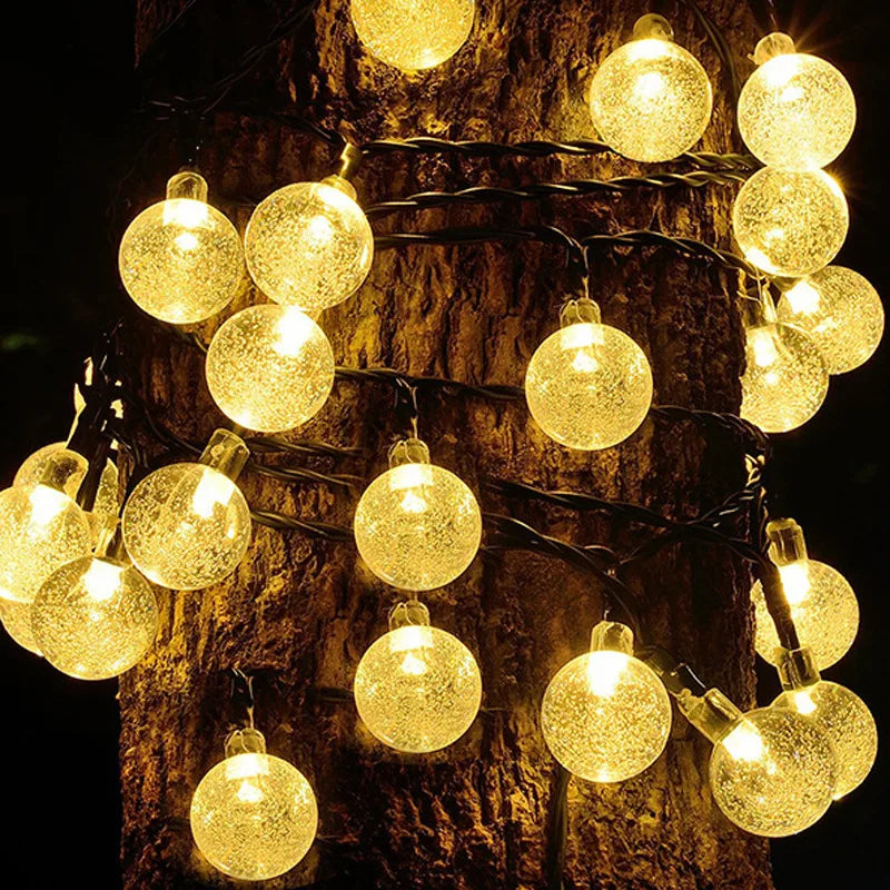A string of round, textured lights emitting a warm glow is wrapped around the trunk of a tree.
