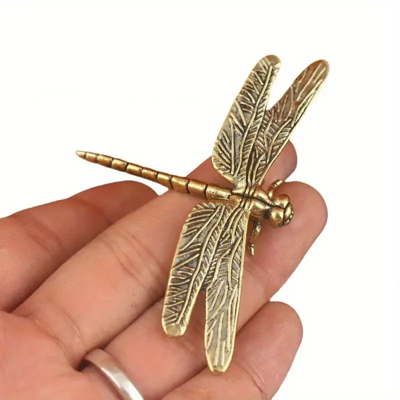 Gold dragonfly-shaped object held in a hand against a white background