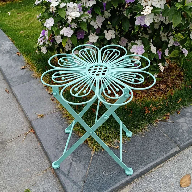 Teal metal folding chair with decorative design on a garden path