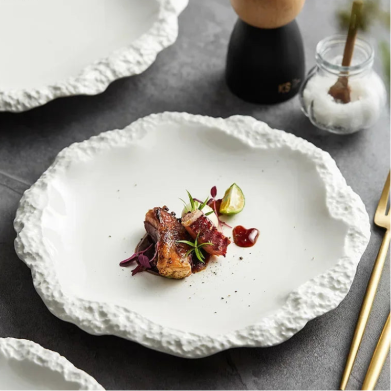 A beautifully plated dish with seared meat and a lime wedge on a white, textured plate.