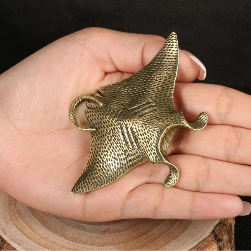 Brass manta ray sculpture held in a hand against a dark background