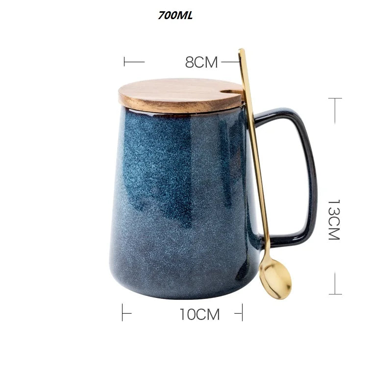 A 700ml ceramic mug with a textured blue glaze, featuring a modern angular handle. The mug has a wooden lid with a small slot for a gold-colored spoon. Dimensions: 13cm in height, 10cm base diameter, and 8cm top diameter.