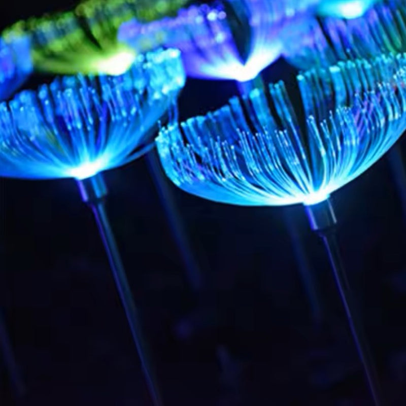 Close-up of several solar-powered garden lights with a jellyfish-like fiber optic design emitting bright blue and green glows at night against a dark background.