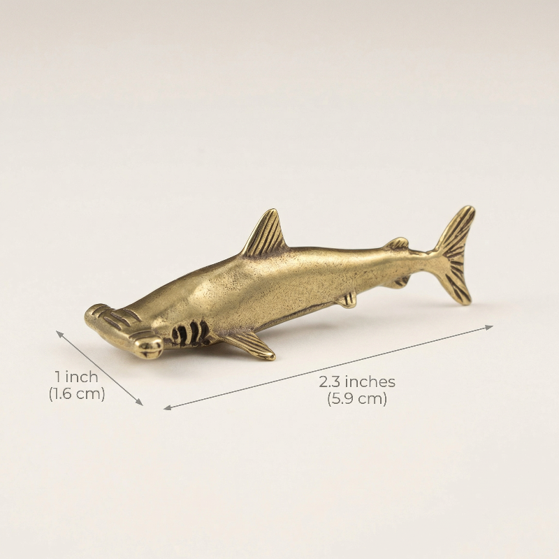 Brass shark figurine with measurements on a light background
