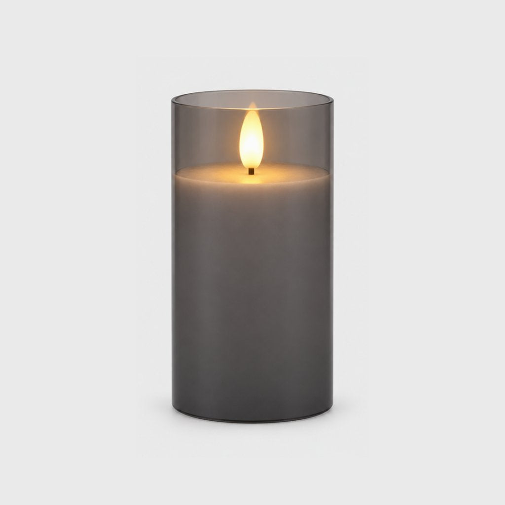 Large grey tinted flameless candle with a glowing flame on a plain light background