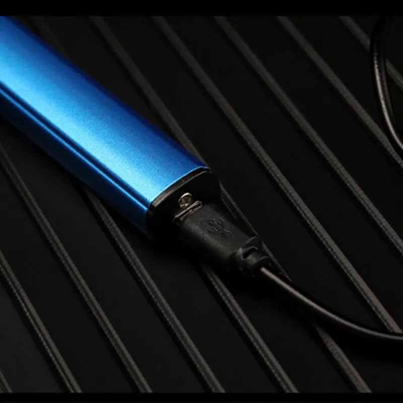 Close-up of a blue electronic device, possibly a lighter, being charged with a black USB cable. The charging port is visible on the side of the device. The background is a black, grooved surface.