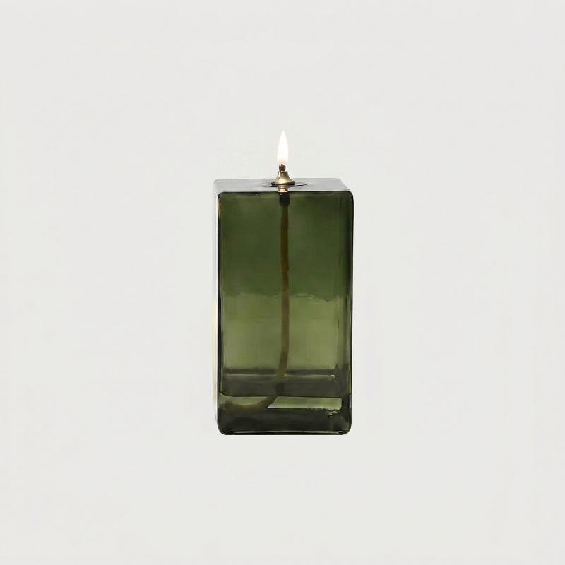 Green glass candle holder with a lit candle on a white background