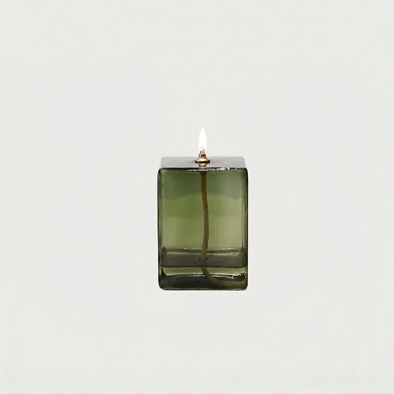Green glass candle holder with a lit candle on a white background