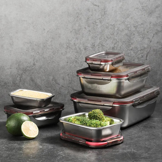 An assortment of stainless steel food containers, some filled with food, arranged on a dark surface.
