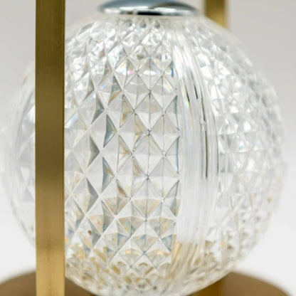A close-up of a lamp's spherical, diamond-patterned glass shade held by a gold metal frame.