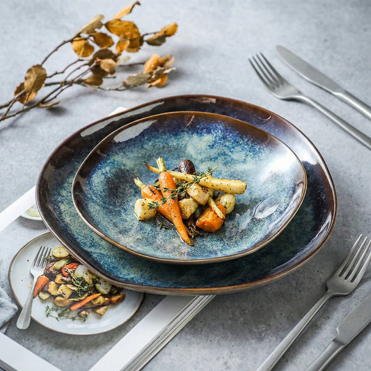 Blue ceramic plate with roasted vegetables on a gray surface with cutlery and decorative elements.