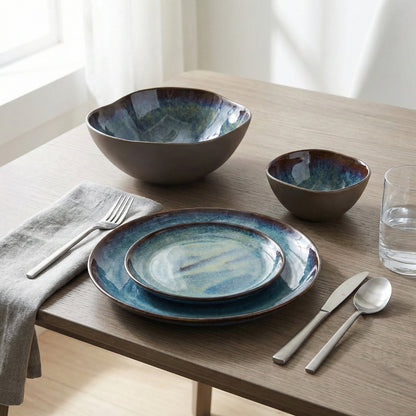Set of ceramic dishes with blue glaze on a wooden table with silverware and a glass.