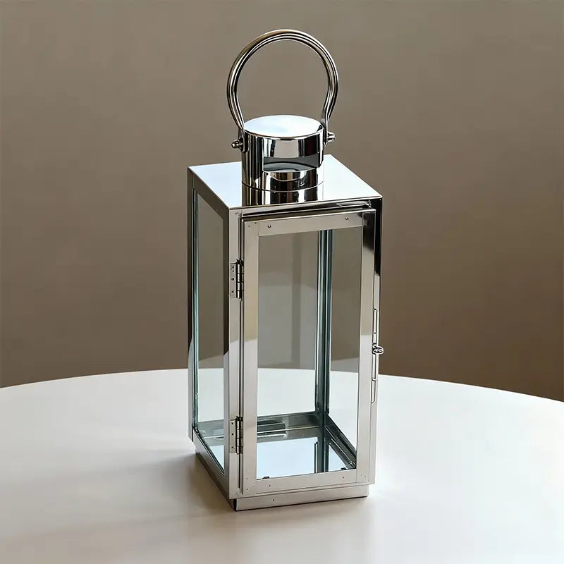 Rectangular silver-toned stainless steel and glass lantern with a handle on a white table.