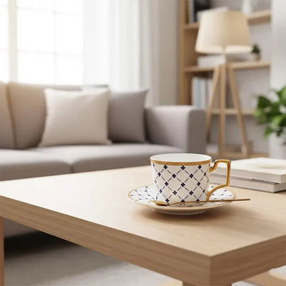White teacup and saucer with blue lattice and clover pattern, gold trim, and a gold spoon on a light wooden coffee table.