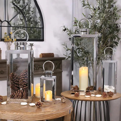 Set of three silver-toned stainless steel and glass lanterns used for decorative display with pinecones and LED candles.
