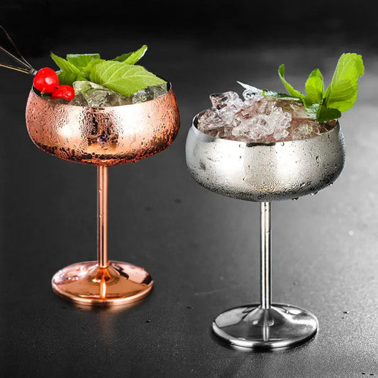 Two chilled metal cocktail glasses, one copper and one silver, filled with ice, mint, and fruit.