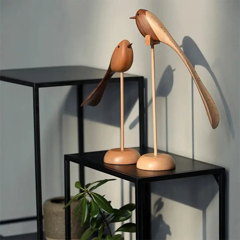 Two decorative wooden bird figurines with long tails on wooden stands are displayed on a black metal tiered shelving unit.