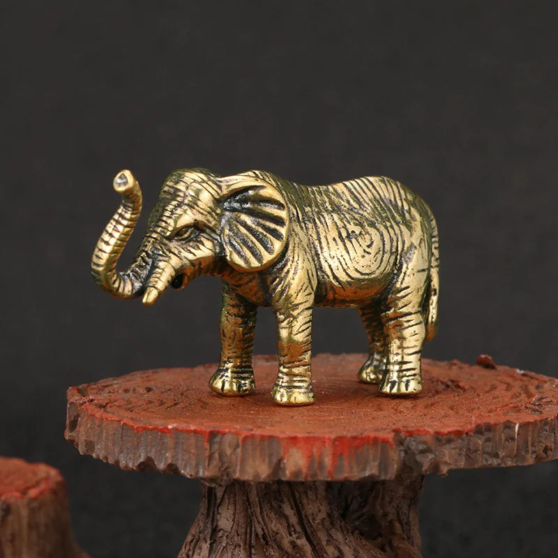 A small, gold-colored elephant figurine with its trunk raised stands on a rustic wooden stand.