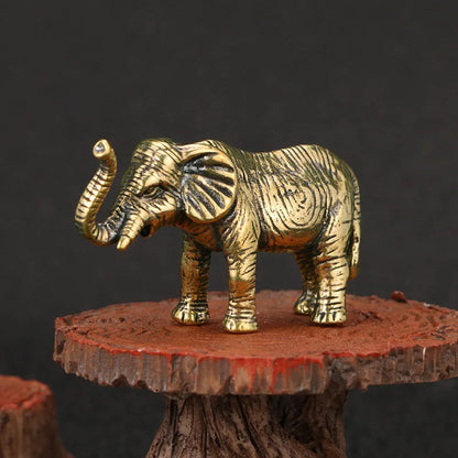 A small, gold-colored elephant figurine with its trunk raised stands on a rustic wooden stand.