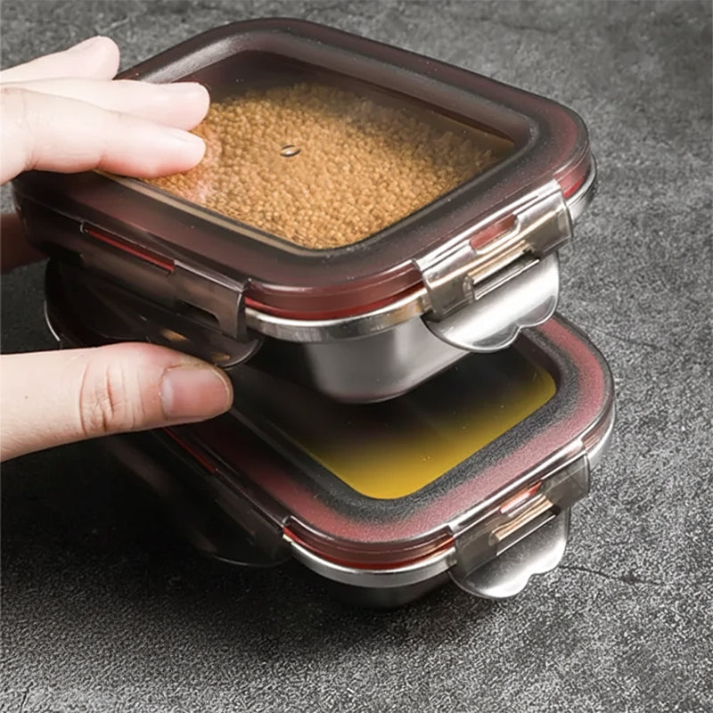 A hand stacks two stainless steel food containers, the top one filled with small brown grains.