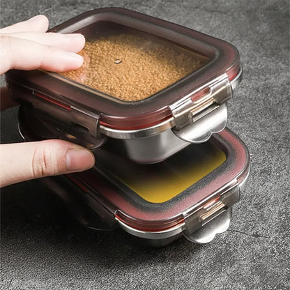 A hand stacks two stainless steel food containers, the top one filled with small brown grains.