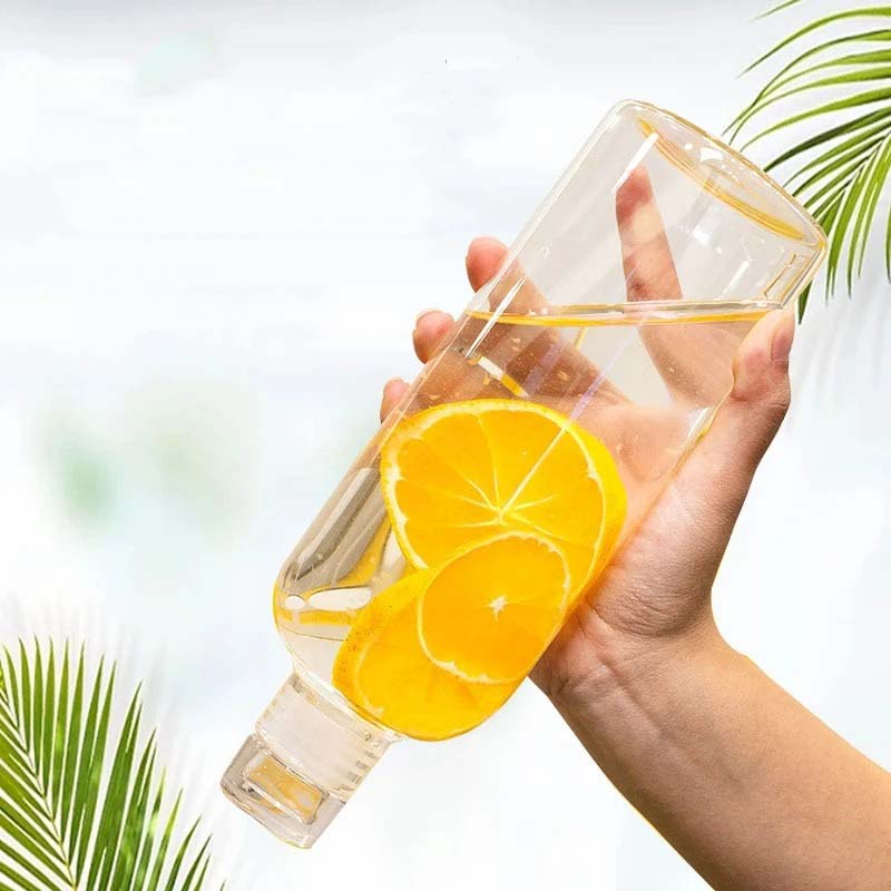 A hand holding a glass bottle with orange slices in water.