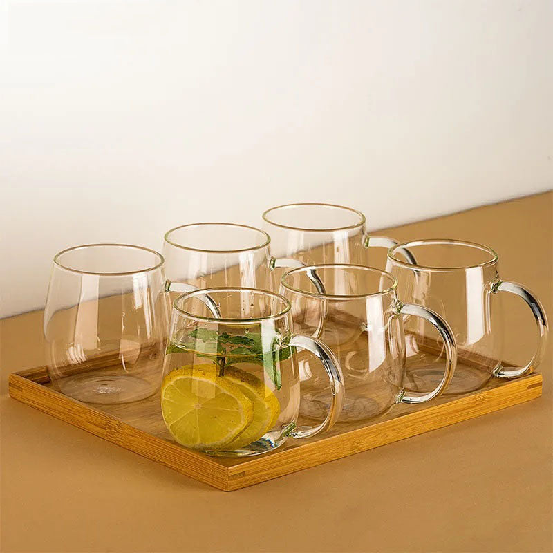 A bamboo tray holds a set of six clear glass mugs, one of which contains lemon slices and mint leaves in a drink.