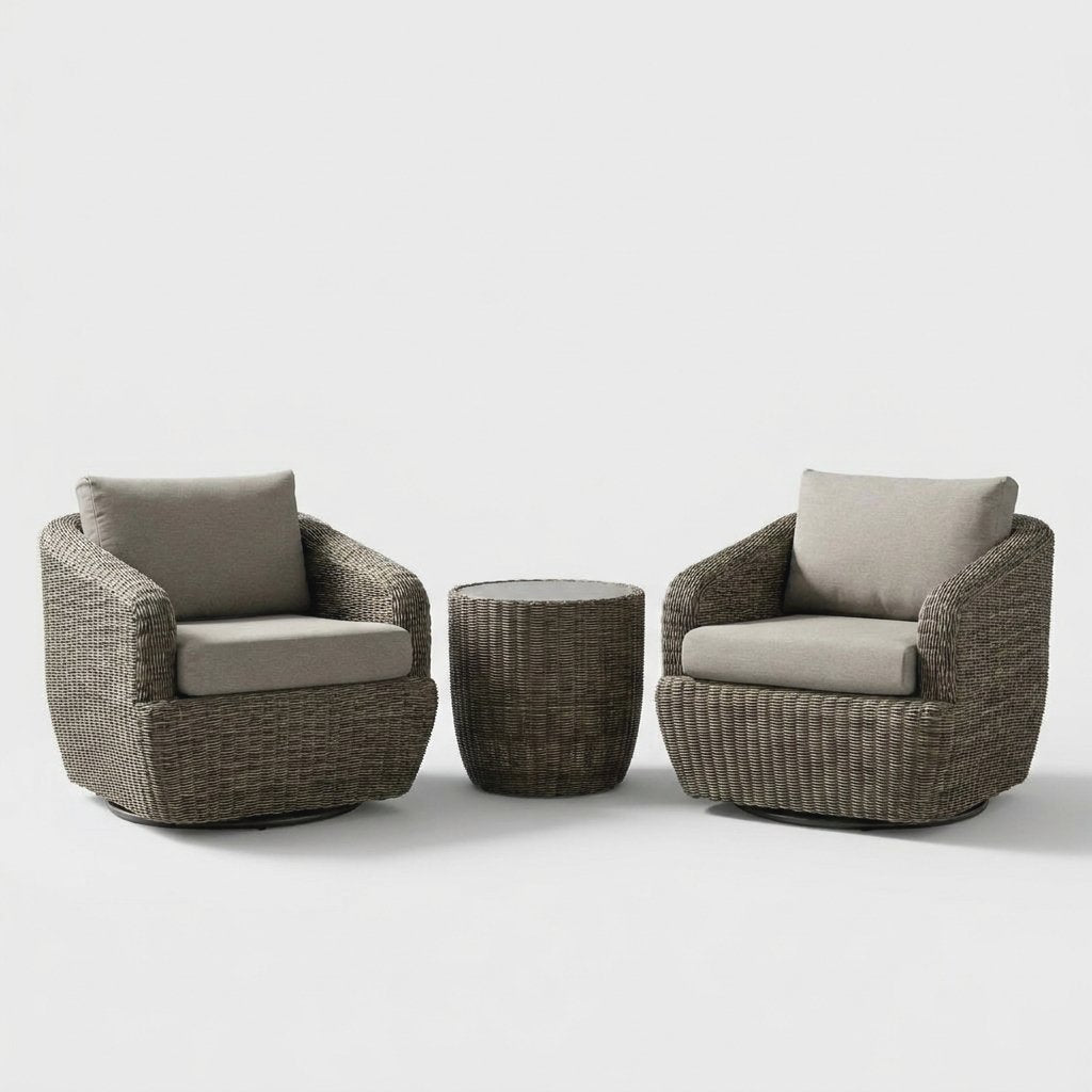 Two gray-brown rattan swivel barrel chairs with greige cushions and dark round swivel bases flanking a round rattan drum table with a pale gray glass top on a plain studio backdrop