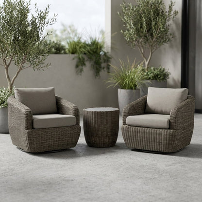 Two gray-brown woven rattan swivel barrel chairs with greige cushions and a round rattan drum table on a concrete patio beside two potted olive trees on an overcast day