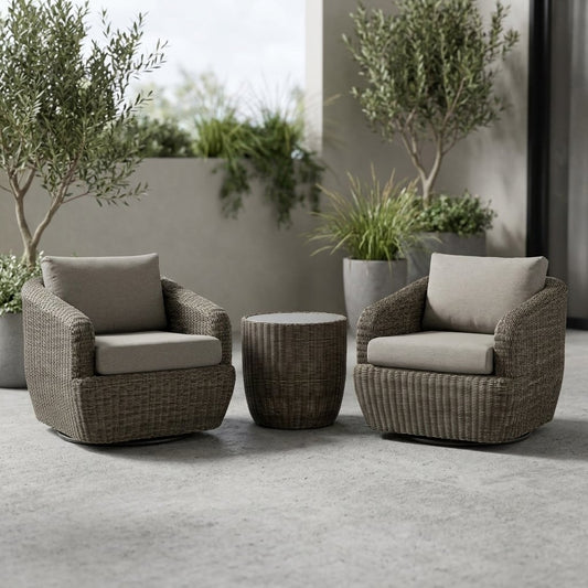 Two gray-brown woven rattan swivel barrel chairs with greige cushions and a round rattan drum table on a concrete patio beside two potted olive trees on an overcast day