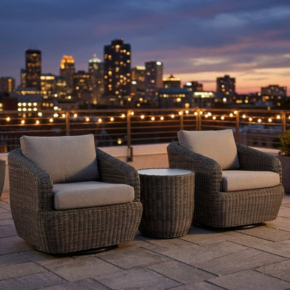 Two gray-brown rattan swivel barrel chairs with greige cushions and a round rattan table on a rooftop with string lights, a metal railing and a city skyline at dusk