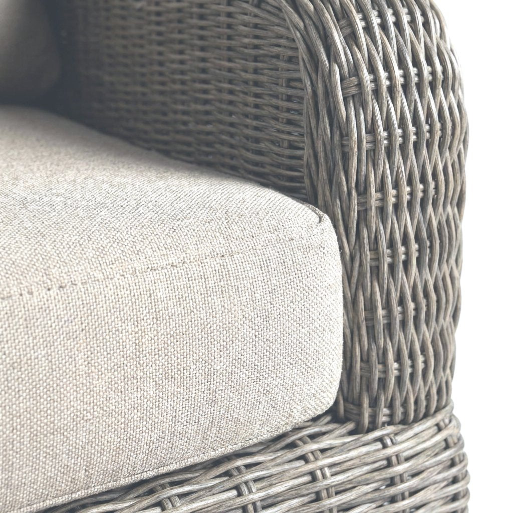 Close-up of the weathered gray-taupe rattan weave on a barrel chair arm with a diamond open weave and a greige cushion on a white background