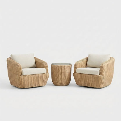 Two honey-tan rattan swivel barrel chairs with cream cushions flanking a round rattan drum table with a dark charcoal glass top on a plain white backdrop