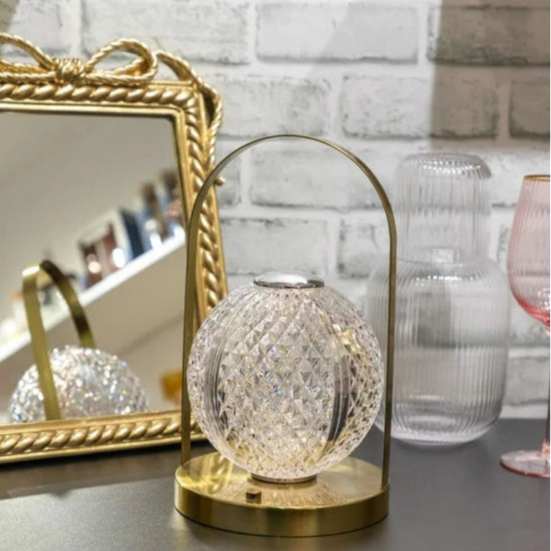 A modern lantern-style lamp with a  patterned, spherical glass shade and a gold-toned metal base and handle