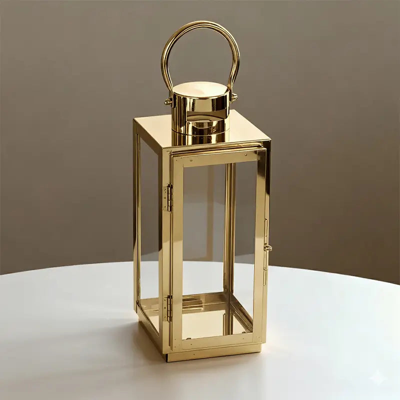 Rectangular gold-toned stainless steel and glass lantern with a handle on a white table.