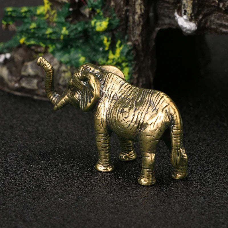 A small, gold-colored elephant figurine with its trunk raised stands on a dark surface, facing away from the viewer.