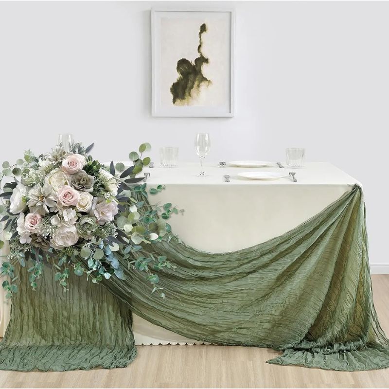 Elegant sage green crinkled table runner draped across a cream-colored table, accented with lush floral arrangements of roses and eucalyptus.