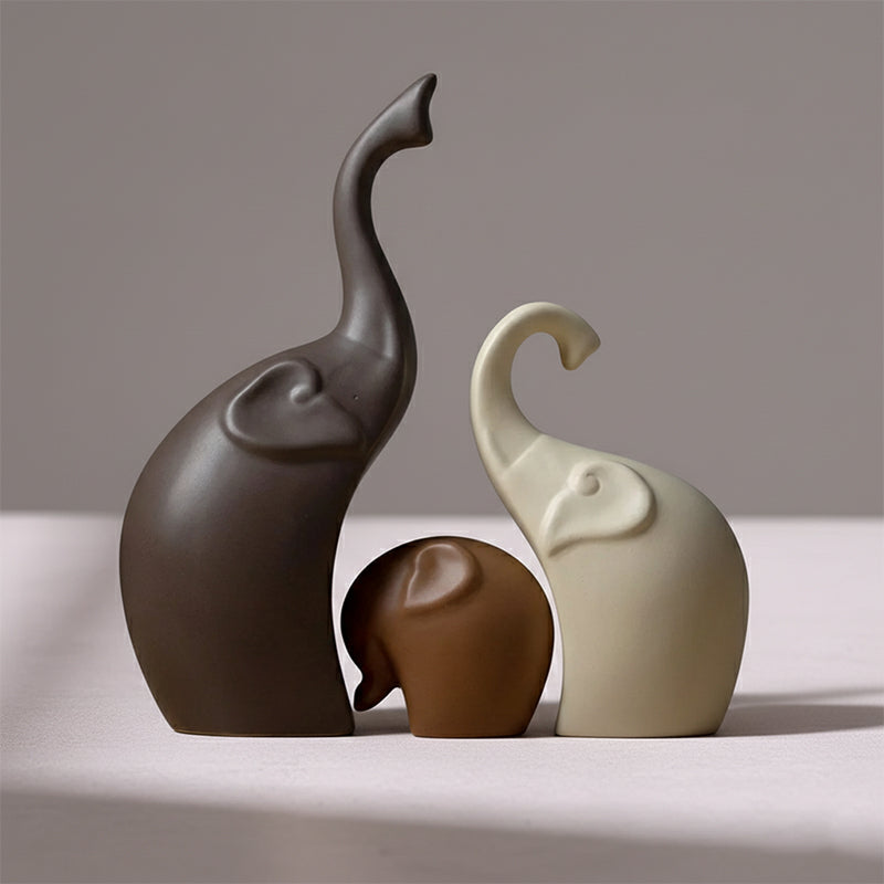 Set of three smooth, minimalist ceramic elephant figurines in shades of brown and cream, with trunks raised.