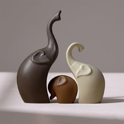 Set of three smooth, minimalist ceramic elephant figurines in shades of brown and cream, with trunks raised.