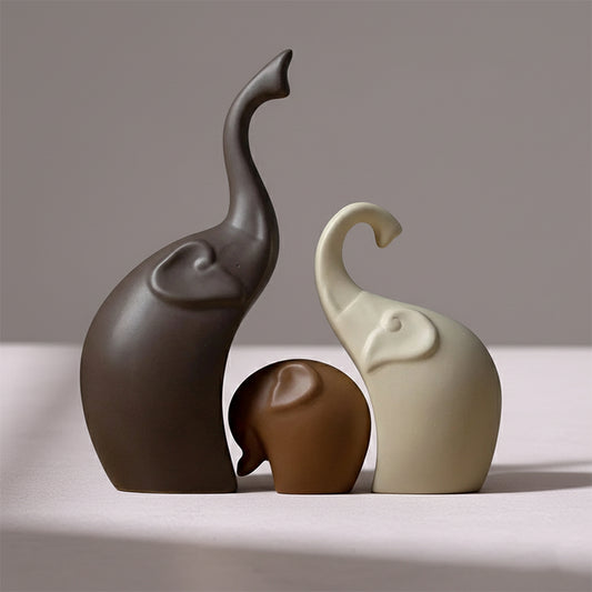 Set of three smooth, minimalist ceramic elephant figurines in shades of brown and cream, with trunks raised.