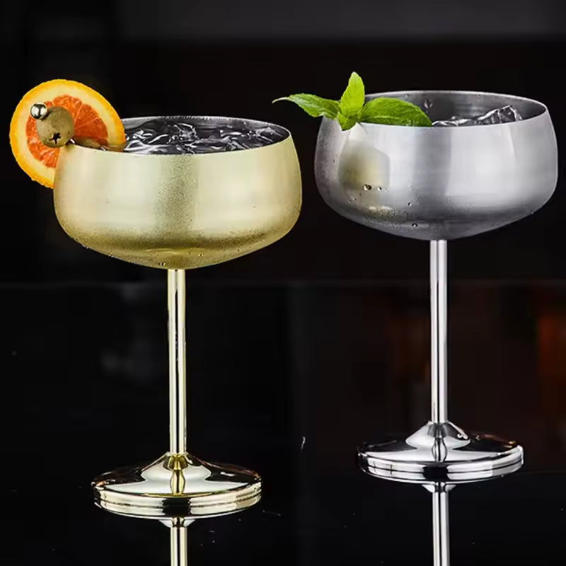 Two cocktail glasses, one gold and one silver, with garnishes on a black background.