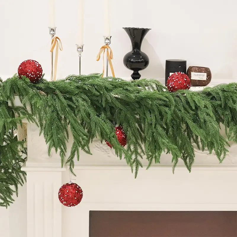 A festive green garland with red ornaments on a mantel.