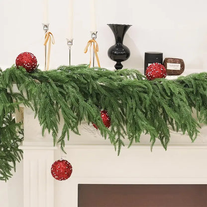 A festive green garland with red ornaments on a mantel.
