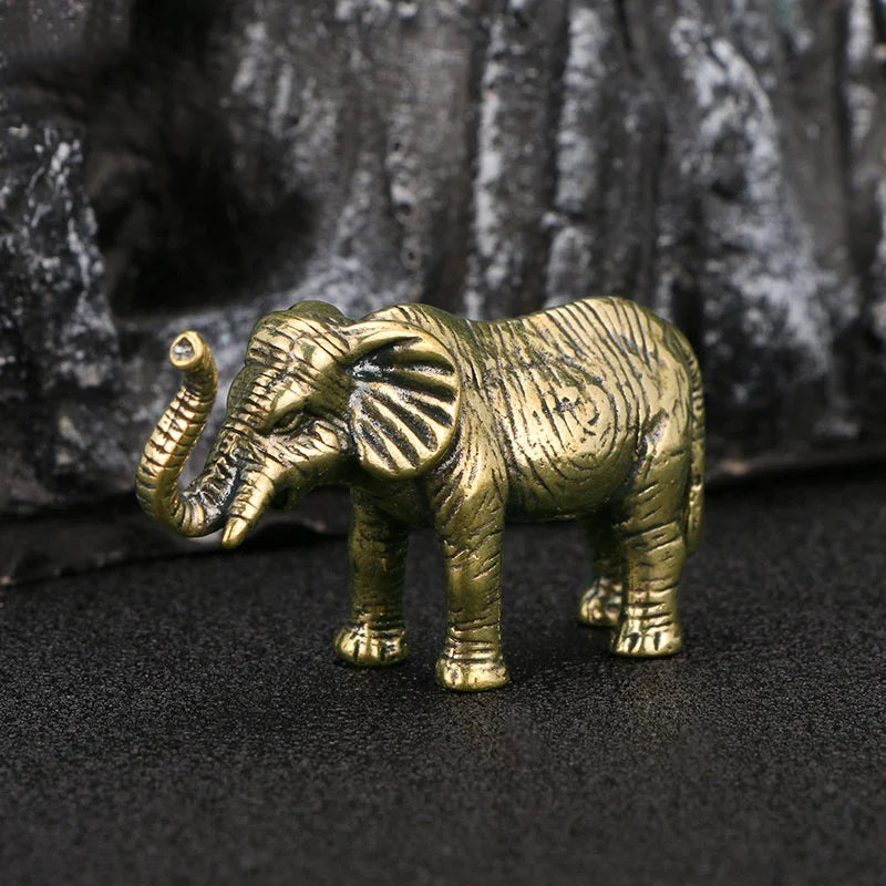 A small, gold-colored elephant figurine with its trunk raised stands on a dark textured surface.