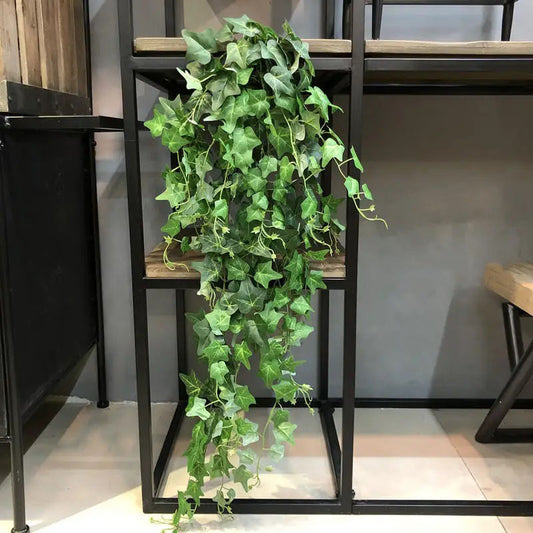 Artificial trailing ivy plant with vibrant green leaves draping from a wooden and black metal shelf.