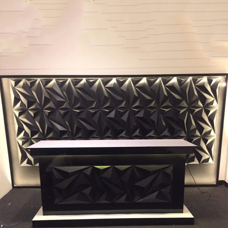 A modern black reception desk in front of a black geometric textured wall panel with backlighting.