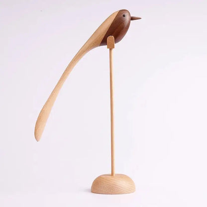 A single decorative wooden bird figurine with a long, sweeping tail, made from contrasting light and dark wood, standing on a thin wooden dowel and round base against a white background.