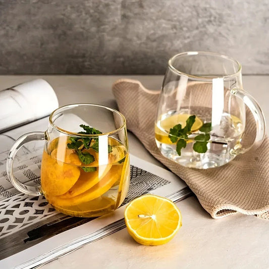 Two glass mugs, each containing a lemon and mint drink, sit on a surface with a magazine and a napkin.