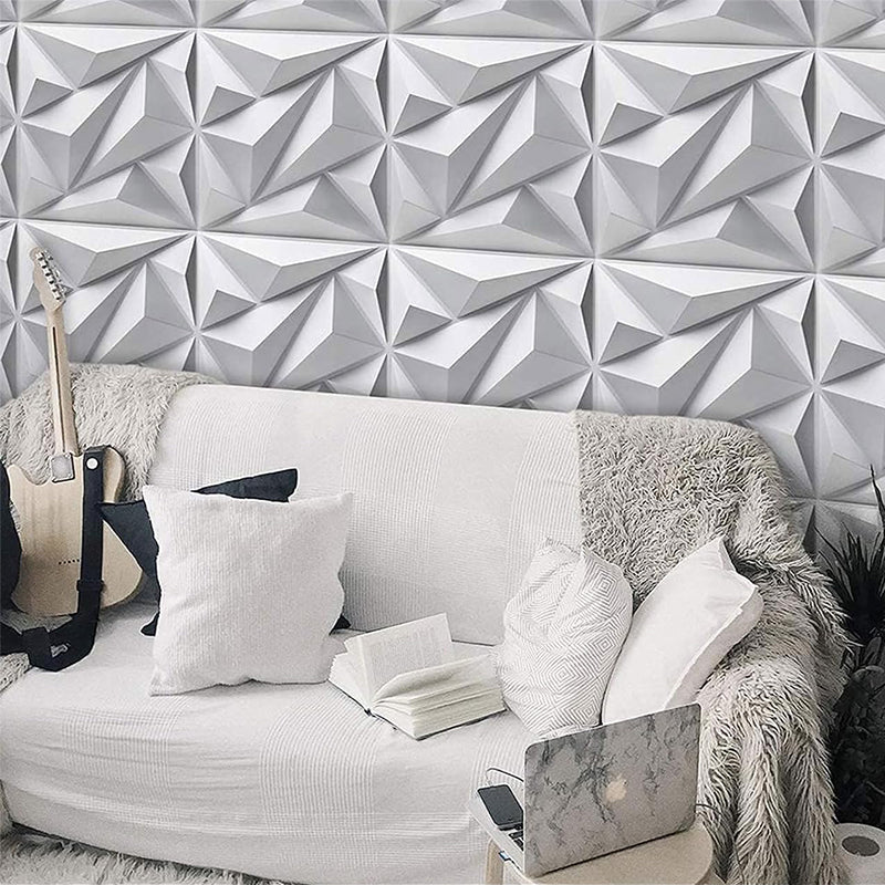 A living room with a white geometric accent wall, a white couch with throw pillows and a fluffy blanket, a laptop, an open book, and a guitar.